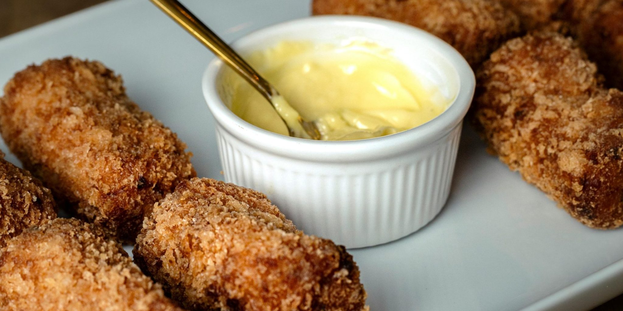 Golden-brown croquettes served with a creamy dipping sauce, perfect for a delicious meal.